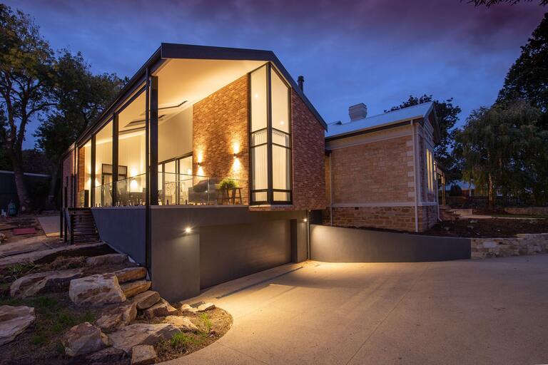 Modernes Haus mit Glasfront am Hang, abends beleuchtet